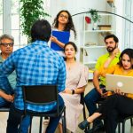Indian Asian young business professionals or startup team receiving a strategic briefing from their team leader in cozy modern office, discussing ideas in a collaborative workspace