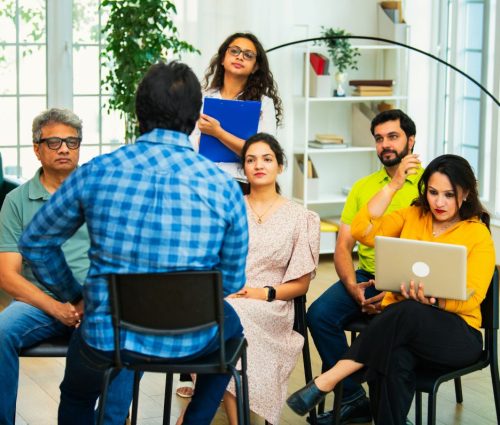 Indian Asian young business professionals or startup team receiving a strategic briefing from their team leader in cozy modern office, discussing ideas in a collaborative workspace